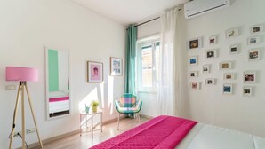 A bedroom with a bed, a tripod floor lamp, a chair, a window with curtains, and a wall with framed pictures. - HOUSE OF MUSIC in Pigneto, METRO C to Colosseo (Roma)