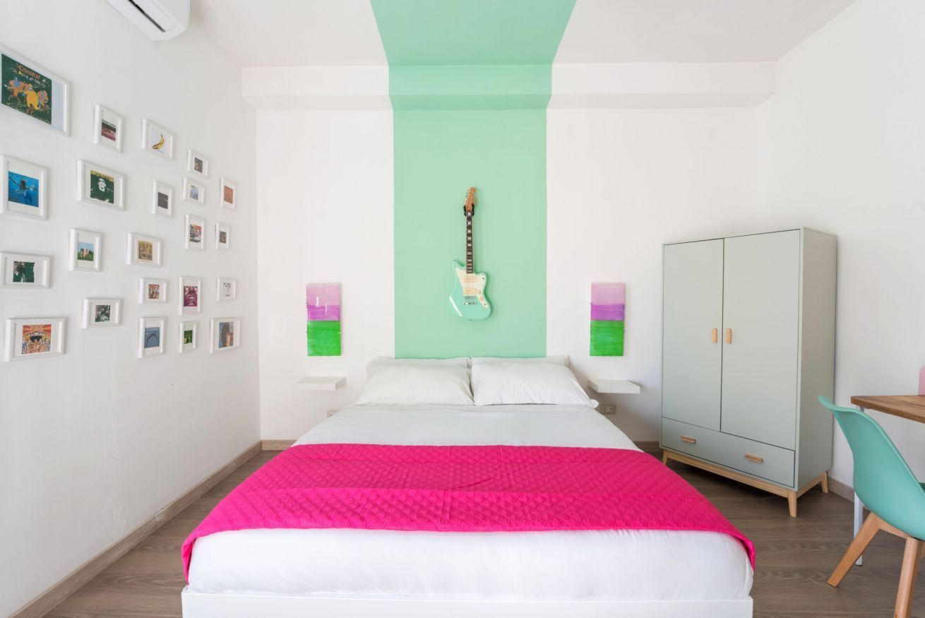 A bedroom with a bed, a guitar, a wardrobe, and a desk.