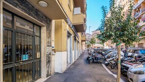 A narrow street with parked motorcycles and cars, a building with a large glass door, and a tree on the sidewalk. - HOUSE OF MUSIC in Pigneto, METRO C to Colosseo (Roma)