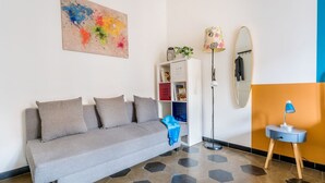 A modern living room with a grey sofa, a colorful abstract painting, a white bookshelf, a floor lamp, and a mirror. - Casetta Giolitti, Cozy Apartment in the Heart of Rome (Roma)