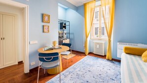 Una habitació amb taula de dinar, cadires, radiador i llit amb edredó rayat.