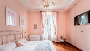 Un dormitori amb llit, cadira, televisió i finestra amb cortines.