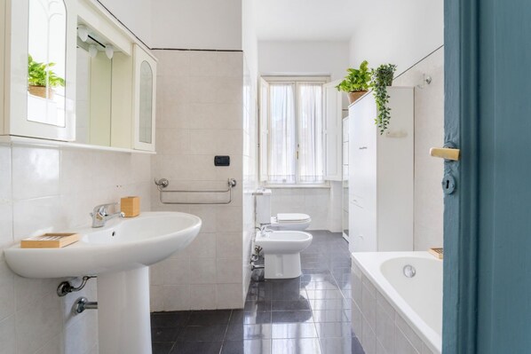 A modern bathroom with a sink, toilet, and bathtub, featuring tiled floors and a window.