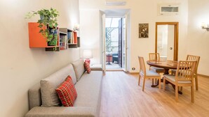 A living room with a sofa, a dining table with chairs, a bookshelf, and a potted plant. - Atelier dello Statuto, a few steps from Colosseo (Roma)
