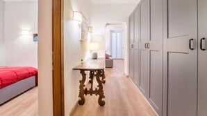 A hallway with a wooden table, a bed with a red cover, and grey cabinets. - Atelier dello Statuto, a few steps from Colosseo (Roma)