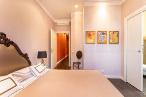 Une chambre d’hôtel avec un grand lit, une table de chevet avec une lampe, une petite table ronde et trois tableaux colorés accrochés au mur.