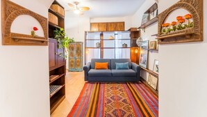 A living room with a sofa, patterned rug, wooden shelves, and decorative items.
