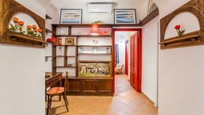 A hallway with a dining area, shelves with framed pictures, and a red door.