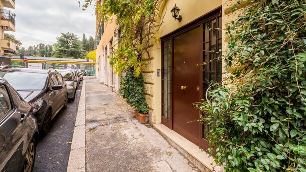 A narrow street with parked cars, a building with a brown door, and a bus in the background.
