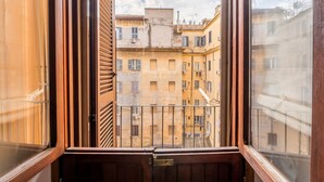 Vista a través de una ventana con marcos de madera, mostrando una hilera de edificios con balcones.