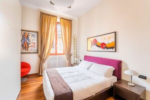 A bedroom with a bed, a nightstand, a lamp, a chair, a window with curtains, and two wall art pieces. - Dimora Esedra, Historical Flat in the Heart of Rome (Roma)