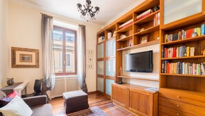 Un salón con sofá, reposapiés, televisor, estanterías de madera y alfombra estampada.