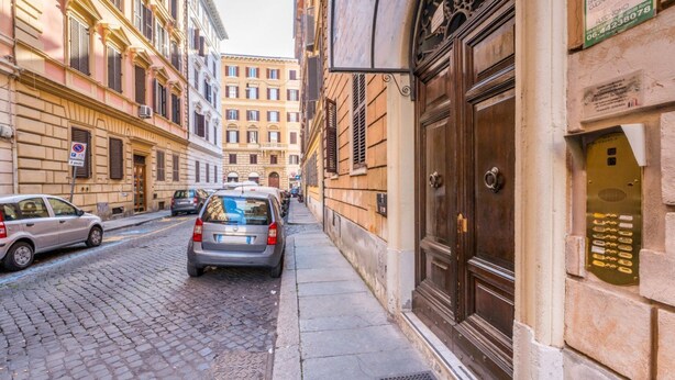 Una calle empedrada estrecha flanqueada por edificios históricos, un coche estacionado y una gran puerta de madera a la derecha.