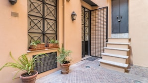Une ruelle étroite, avec un portail en métal, un escalier et des plantes en pot.