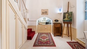 Un couloir avec un escalier, un tableau posé sur un chevalet et une moquette rouge.