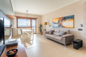 A modern living room with a sofa, dining table, and a large window offering a city view.