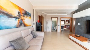 A modern living room with a sofa, a large abstract painting, and a kitchen in the background. - Cielo Suite, Panoramic View Apt with Jacuzzi (Roma)