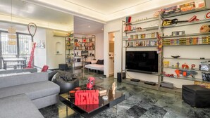 A modern living room with a sofa, coffee table, and a TV. There is a bookshelf filled with books and toys. - Comics Roma Penthouse, Funny Flat Nearby Colosseum (Roma)