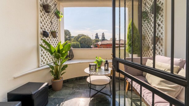 A balcony with a glass door, potted plants, a round table, and a cushioned seating area. - Comics Roma Penthouse, Funny Flat Nearby Colosseum (Roma)
