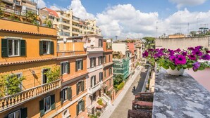 A row of multi-story buildings with balconies, a clear sky, and a potted plant with purple flowers on the right. - Elizabeth Penthouse, Charmy Penthouse in Little London (Roma)
