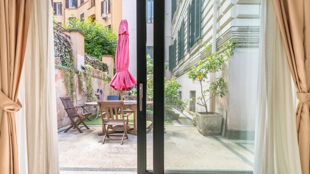A room with a sliding glass door leading to an outdoor patio with a table, chairs, and a pink umbrella. - Flaminio Garden, Indenpent Apt in Piccola Londra Street with Garden (Roma)