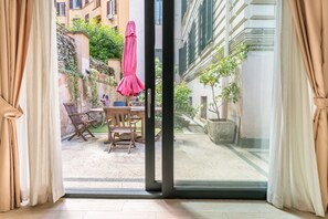 A room with a sliding glass door leading to an outdoor patio with a table, chairs, and a pink umbrella. - Flaminio Garden, Indenpent Apt in Piccola Londra Street with Garden (Roma)