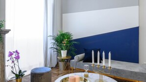 A modern living room with a blue accent wall, a round coffee table with candles, a potted plant, and a sofa with cushions. - GLAM 50 - Exclusive Penthouse in the Heart of Rome (Roma)