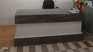Balcão de recepção com parede de grama artificial verde, parede de azulejos brancos e chão xadrez.