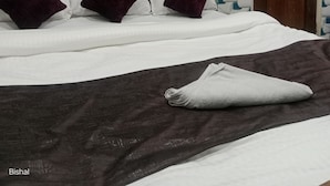 Quarto de hotel com uma cama, porta de madeira e janela com cortinas.