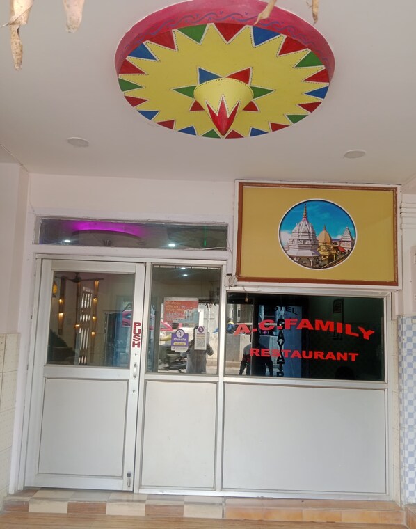 A restaurant entrance with a colorful ceiling design, a framed picture of a temple, and a glass door with a sign reading "A-C Family Restaurant". - Hotel gayatri  (Nalbari)