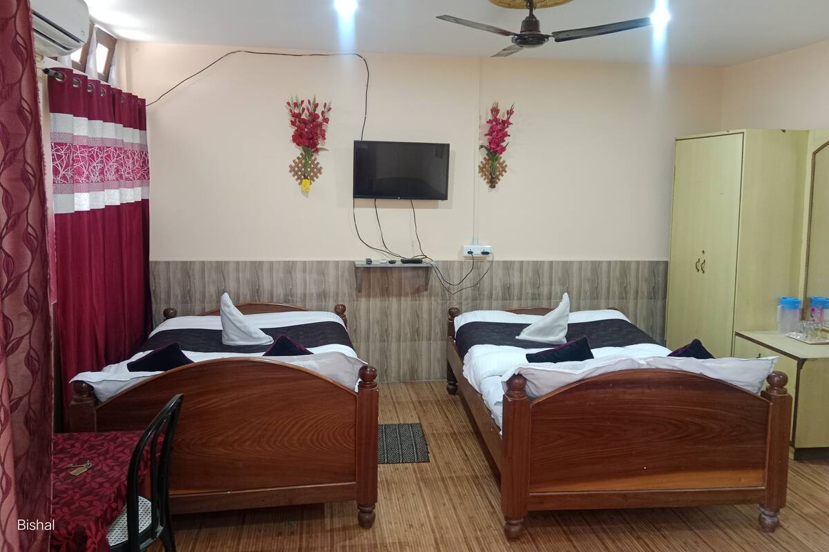 Habitación de hotel con dos camas de madera, un ventilador de techo, un televisor montado en la pared y un armario.