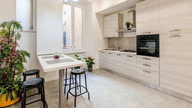 A modern kitchen with light wood cabinets, a black stove, and a window overlooking the city. - Home of Arts, Concept apt in the Center of Rome (Roma)