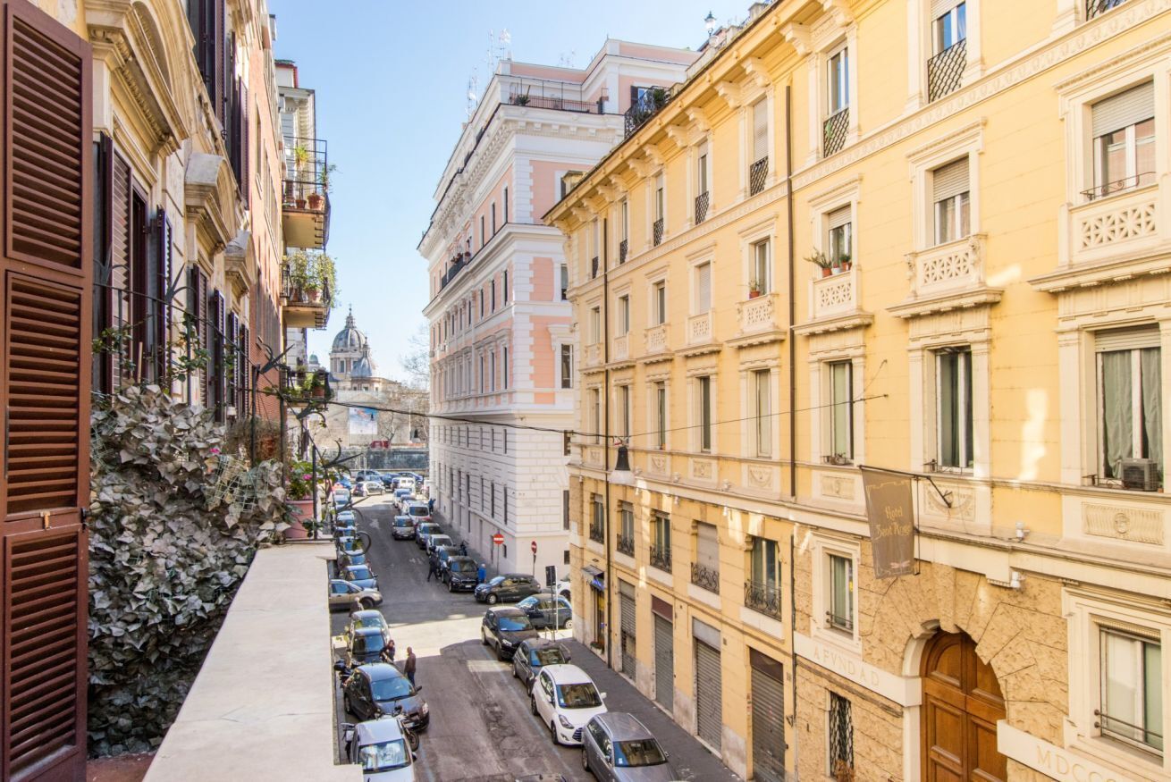 A street view with parked cars, buildings with balconies, and a clear sky.