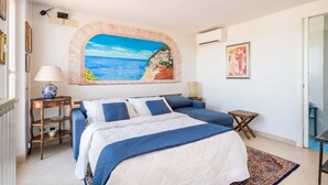 Un dormitorio con una cama, un cuadro de una playa, una mesita y una silla.