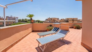 Terraza en la azotea con dos sillones a rayas, una planta en maceta y una vista despejada de los edificios circundantes.