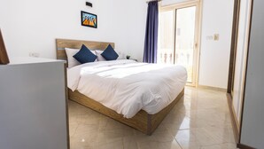 Una cama bien hecha con estructura de madera y ropa de cama blanca, una mesita de noche pequeña y un cuadro en la pared.