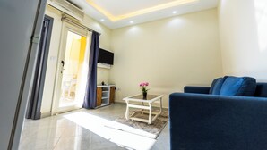 Un salón con sofá, una mesita con un jarrón de flores, televisor montado en la pared y una puerta corredera que da a un balcón.