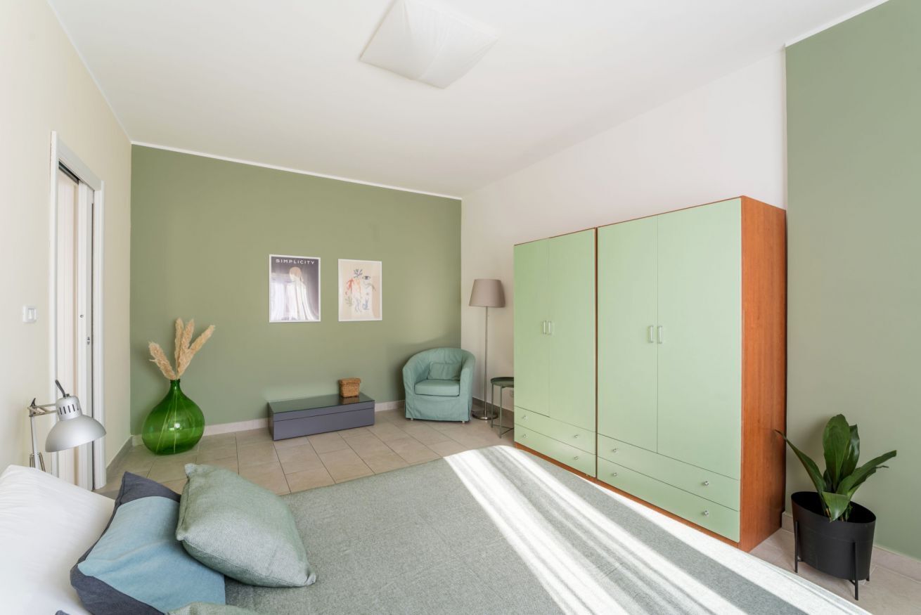 A room with a bed, a green sofa, a green cabinet, a lamp, a vase, and a plant.