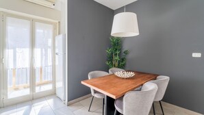 Un comedor con una mesa de madera, sillas grises, una lámpara colgante blanca y una planta en maceta.