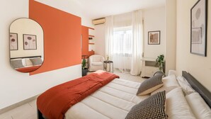 Un dormitorio con una cama, una silla, una mesita y un espejo.
