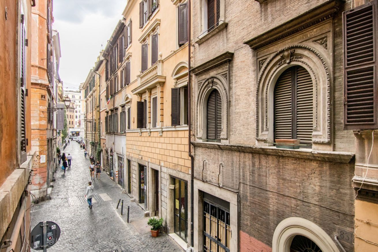 Una estrecha calle adoquinada flanqueada por edificios históricos con ventanas arqueadas y contraventanas.