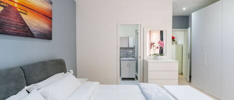 A modern bedroom with a bed, a painting, a bathroom, and a kitchenette.