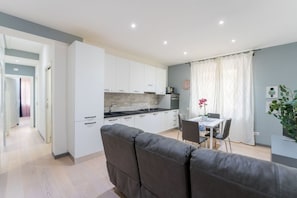 Una cocina moderna con armarios blancos, un comedor con mesa y sillas, y un sofá gris en primer plano.