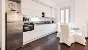 A modern kitchen with white cabinetry, stainless steel appliances, and a dining area with white chairs. - The Vatican Rest, Elegant Apt Nerby the Basilica (Roma)