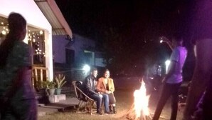 An outdoor seating area with a fire pit, surrounded by potted plants and a building with a porch. - Sneha Homestay by Roh (Bokakhat)