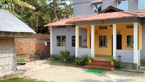 A two-story building with a red-tiled roof, a porch with steps, and a garden area with potted plants. - Sneha Homestay by Roh (Bokakhat)