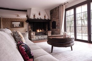 A cozy living room with a stone fireplace, a large window, and a comfortable sofa. - Exceptional Alsatian estate with private lake (Rountzenheim-Auenheim)