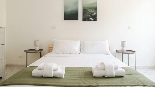A hotel room with a bed, two nightstands, a green area rug, and two wall-mounted paintings. - Casa Vic Garbatella in Rome (Rome)
