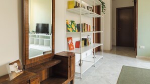 A room with a wooden desk, a large mirror, a white shelving unit with books and decorative items, and a door in the background. - Casa Vic Garbatella in Rome (Rome)