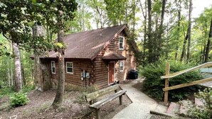 Eine rustikale Blockhütte mit einer Holzbank und einem Betonweg, der zur Tür führt.